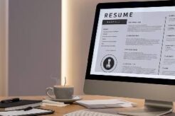 Imagem de um ambiente de trabalho moderno e organizado com um computador mostrando um modelo de currículo na tela, acompanhado de itens de escritório como caneta, caderno e uma xícara de café.